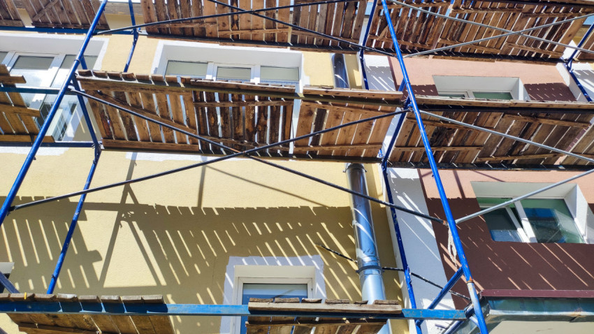 Фасад здания со строительными лесами, окнами и металлической водосточной трубой
