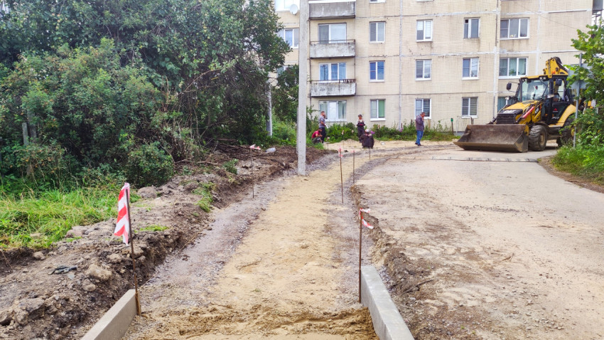 Подготовка основания под новую дорожку у жилого дома с участием рабочих и экскаватора-погрузчика