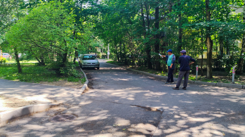 Тенистый дворовой проезд с зеленью и людьми, обсуждающими состояние дороги