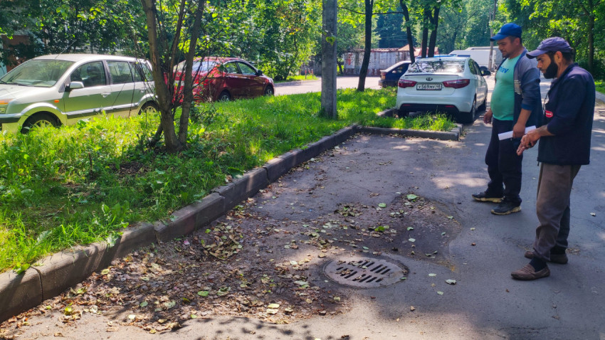 Осмотр дворового покрытия: мужчины с документами указывают на проблемный участок у люка