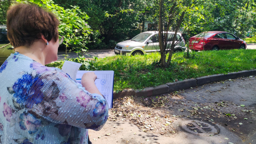 Женщина с документами указывает на участок дворового проезда рядом с люком ливнёвки