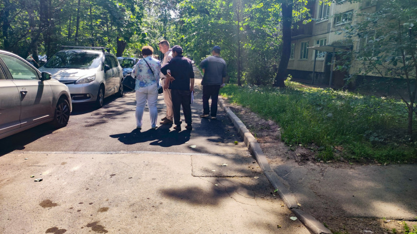 Группа жителей обсуждает вопросы двора рядом с припаркованными автомобилями и жилым домом