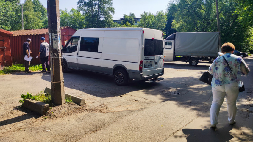 Грузовой фургон и люди с документами на дворовом проезде рядом с гаражами