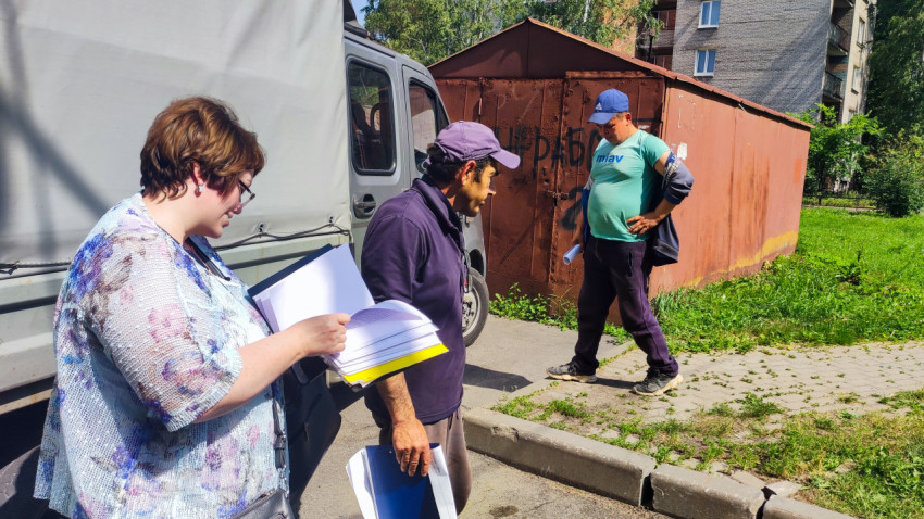 Сотрудники обсуждают документы у грузовика на фоне дворовых гаражей и жилого дома