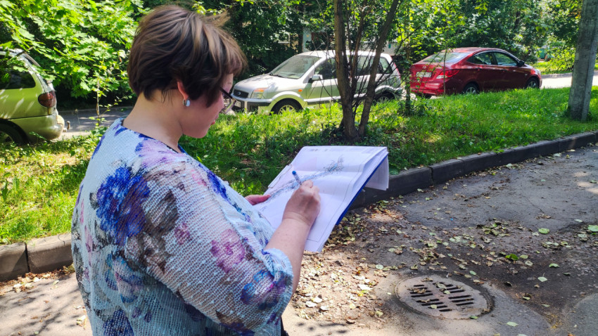 Женщина заполняет документы во дворе жилого дома рядом с припаркованными автомобилями