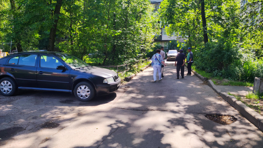 Жители идут по дворовому проезду среди деревьев и припаркованных автомобилей