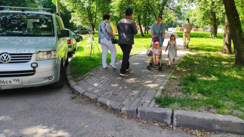 Семья с коляской проходит по плиточной дорожке рядом с припаркованным Volkswagen