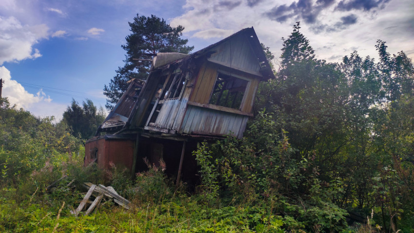 Фасад заброшенного деревянного дома с пустыми оконными проёмами и обломками досок