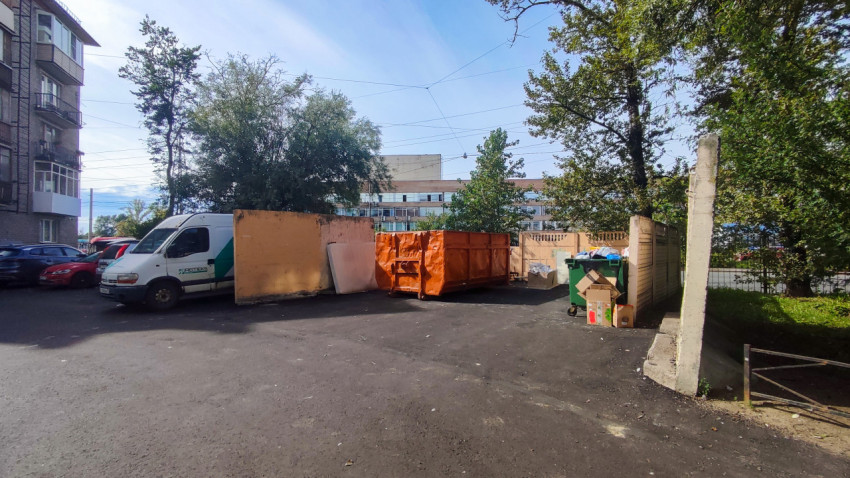 Контейнерная площадка во дворе с мусорными баками и большим оранжевым контейнером для вывоза отходов