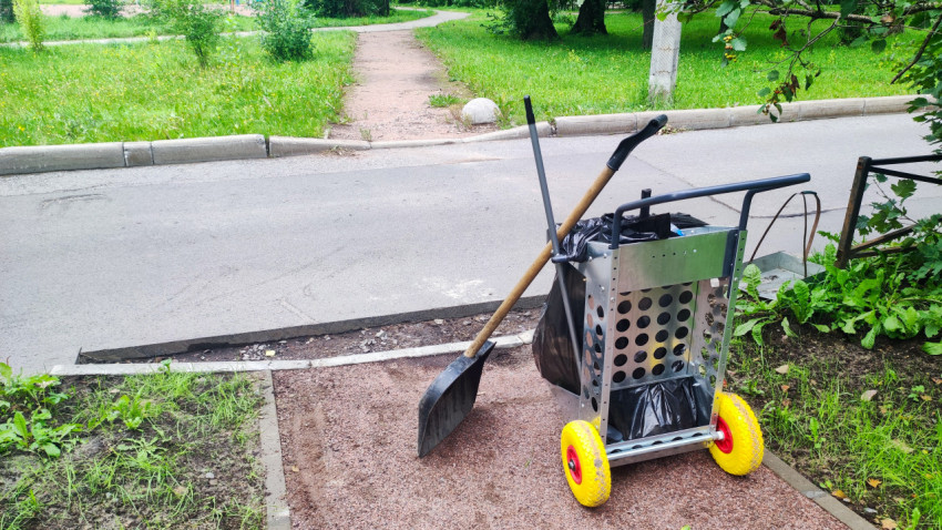 Тележка дворника с инструментами и мешками для мусора у тротуара