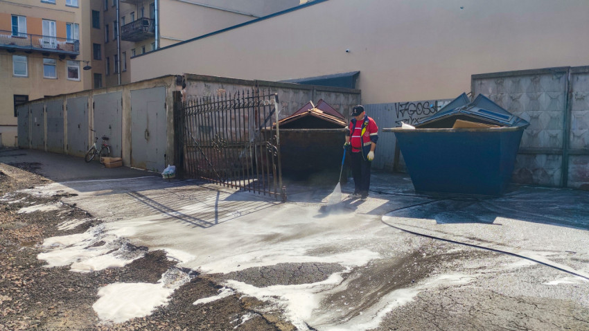 Рабочий моет асфальт струёй воды и пеной рядом с контейнерами и гаражными воротами