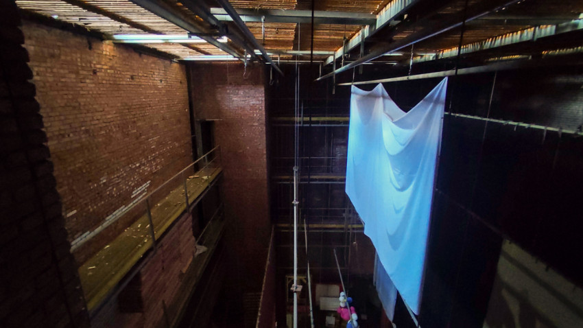 Высокий кирпичный зал с металлическими балками, галереей и подвешенным белым полотном