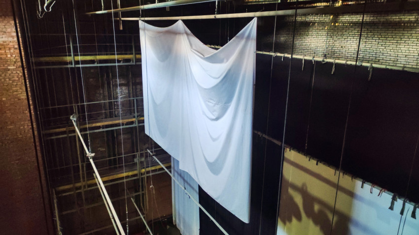 Белое полотнище на подвесах и тросах на фоне кирпичной стены и чёрных кулис