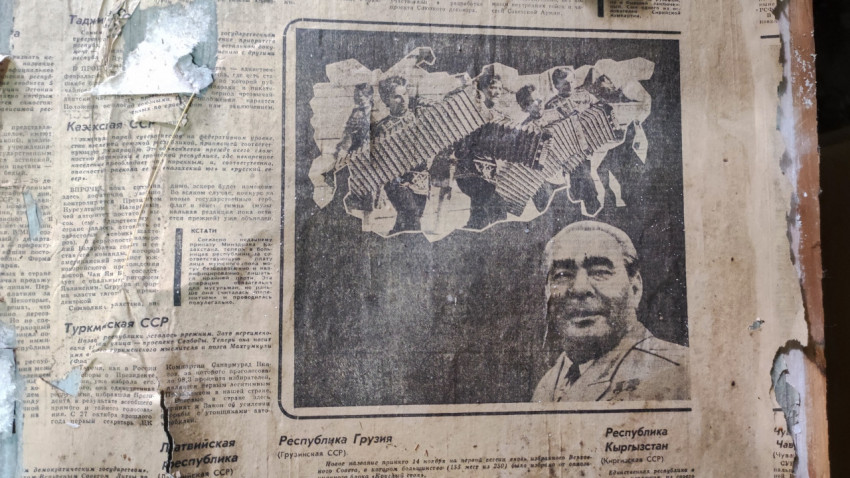 Кусок старой газеты с советской печатью и портретом на стене выглядит как винтажный фон