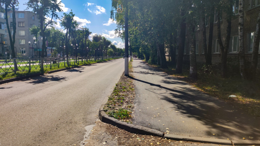 Перспектива жилой улицы с тротуаром, ограждением и рядами деревьев в солнечную погоду