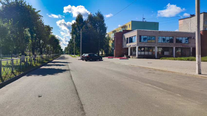 Городская улица с аллеей деревьев и торговым зданием с вывеской «Градусы»