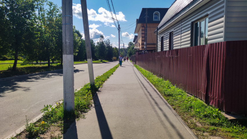 Тротуар вдоль дороги с деревянным забором, столбами и проводами в жилом районе