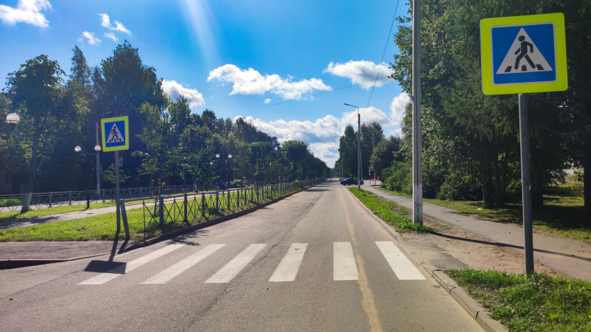 Пешеходный переход на городской улице с ограждением, знаками и зелёной обочиной