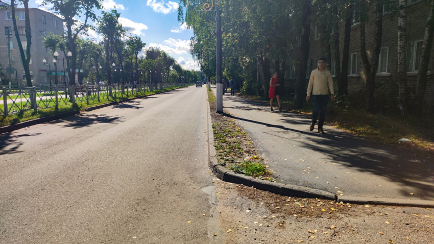 Пешеходы на тротуаре вдоль зелёной аллеи на городской улице у жилых домов