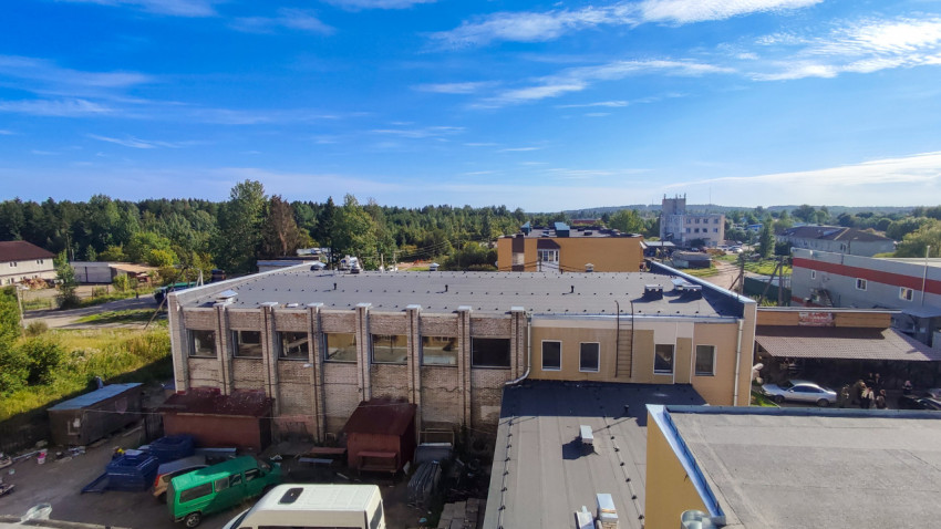 Промышленное здание с плоской крышей и дворовой территорией на фоне леса в летний день