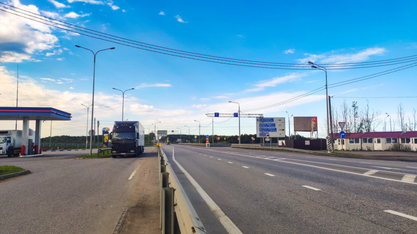 Автомагистраль с развязкой, дорожными указателями, грузовиком и автозаправкой при ясном небе