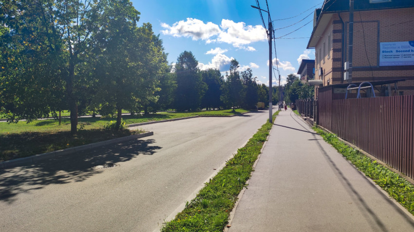 Дорога и тротуар вдоль зелёной зоны рядом с жилым домом и забором