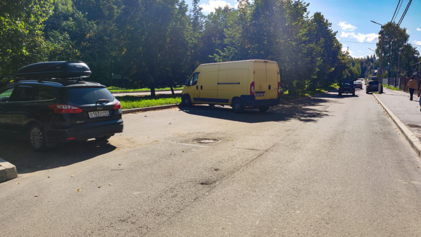 Припаркованные автомобили у обочины и люк колодца на асфальте городского проезда