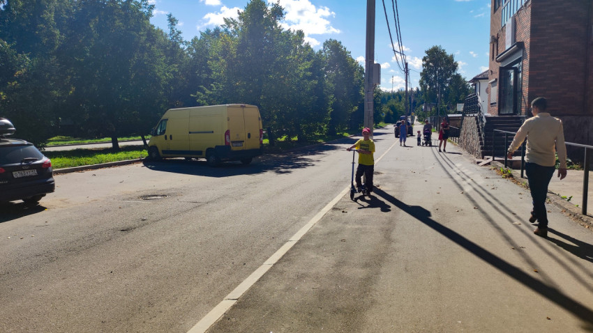 Ребёнок на самокате и пешеходы на тротуаре городской улицы в жилом районе