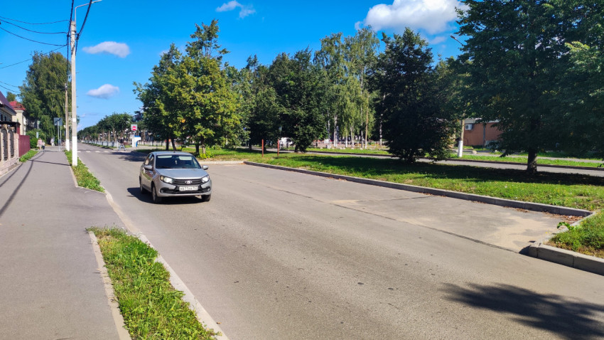 Легковой автомобиль на городской дороге рядом с тротуаром и деревьями в ясную погоду