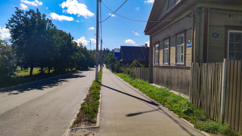 Улица частного сектора с асфальтовой дорогой, тротуаром и деревянным домом у обочины