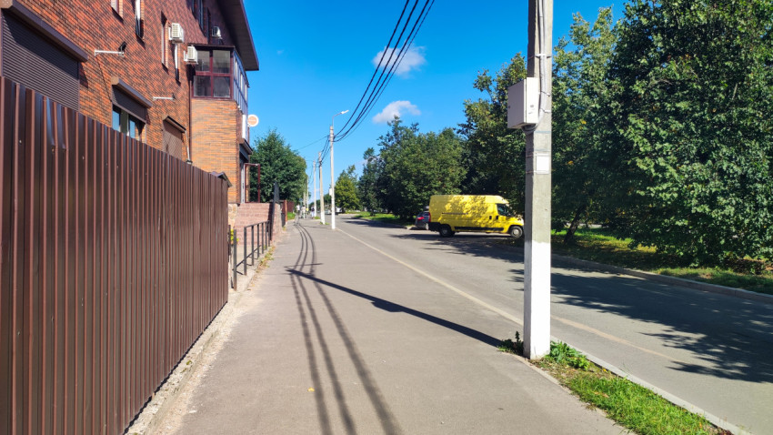 Тротуар у металлического ограждения с опорой и проводами на улице жилого района