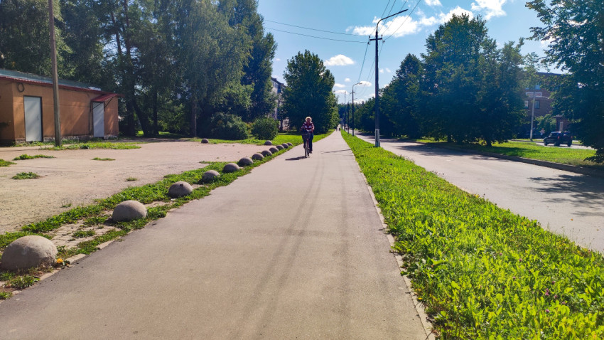 Велосипедист едет по тротуару вдоль дороги и зелёной зоны