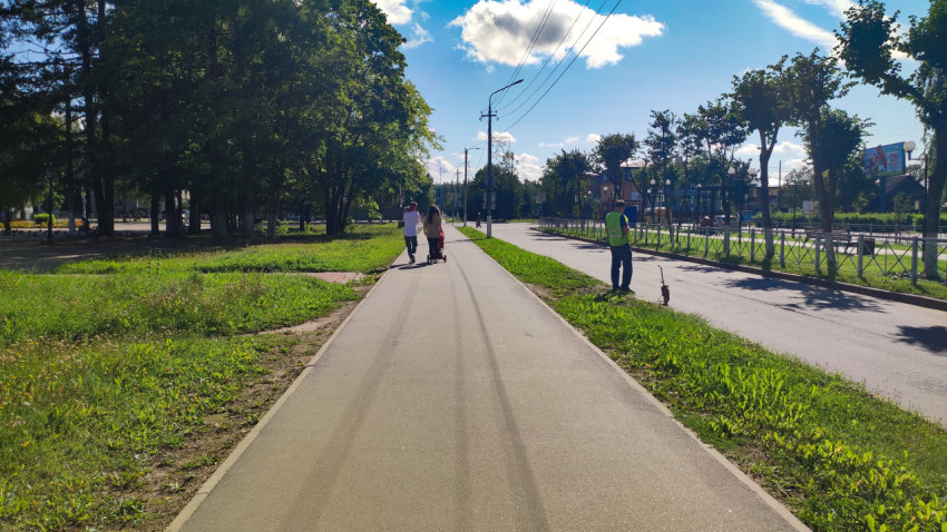 Прямая дорожка в парке: гуляющие люди, газон и рабочий с измерительным колесом у края