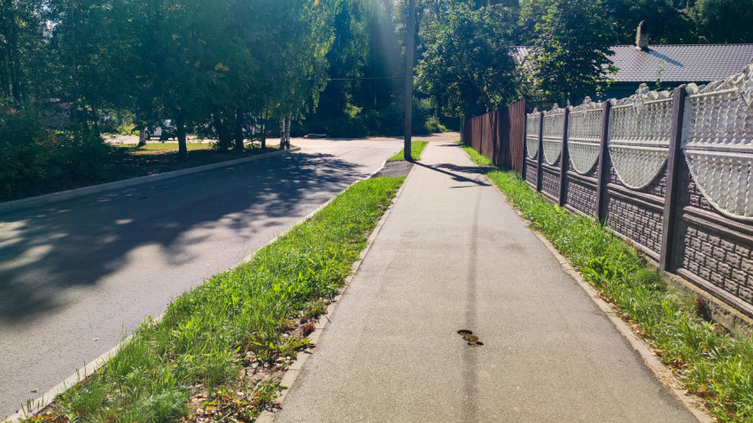 Отверстия от кернирования на асфальтовом тротуаре рядом с дорогой и частным забором