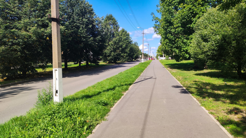 Тротуар у дороги с травяной полосой, столбом и проводами над улицей