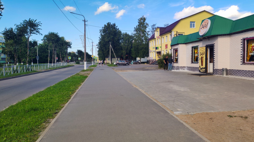 Кафе «Зира» у дороги, а у входа стоят люди и горит рекламная подсветка в окнах