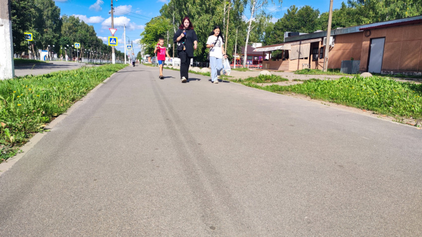 Люди идут по тротуару вдоль проезжей части в жилом районе