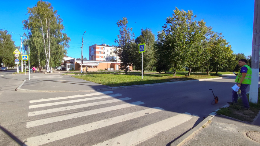 Рабочий у пешеходного перехода держит документы, а измерительное колесо стоит на асфальте