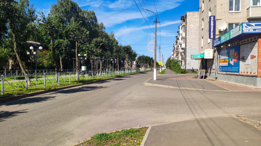 Улица с парковой оградой и фонарями слева и фасадами домов с витринами справа