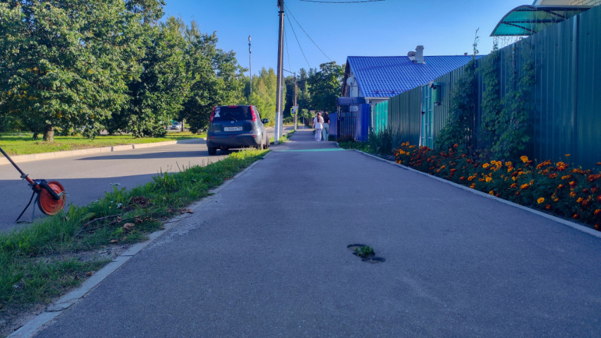 Яма и просадка на тротуаре рядом с клумбой и зелёным забором