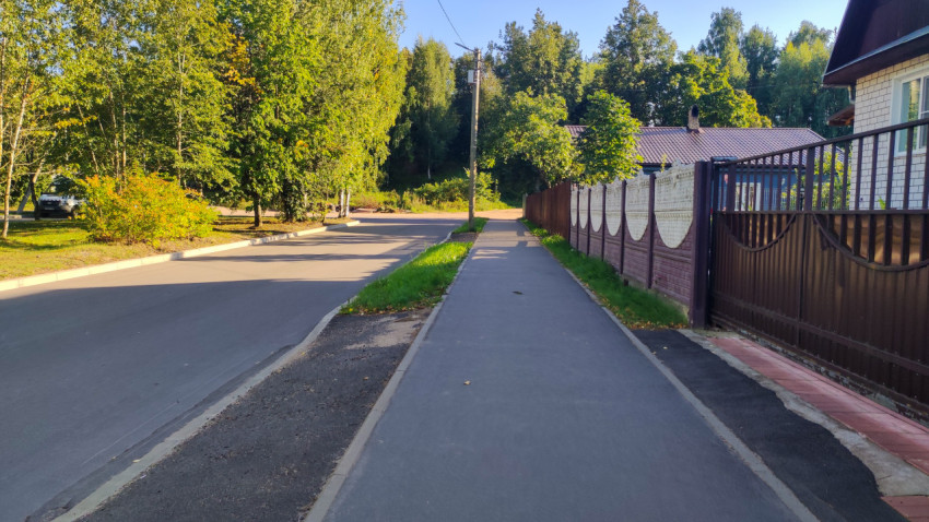 Тротуар вдоль дороги рядом с забором и воротами частного дома