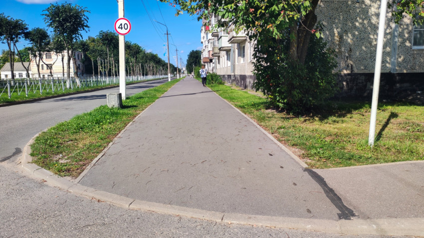 Знак ограничения скорости 40 стоит у тротуара на тихой улице рядом с деревьями и заборами