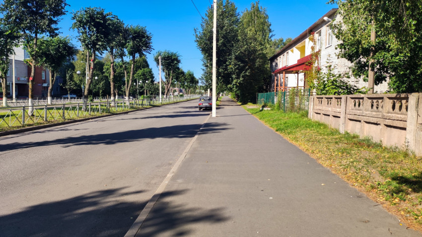 Улица с тротуаром, опорами и проводами рядом с жилыми домами и ограждением