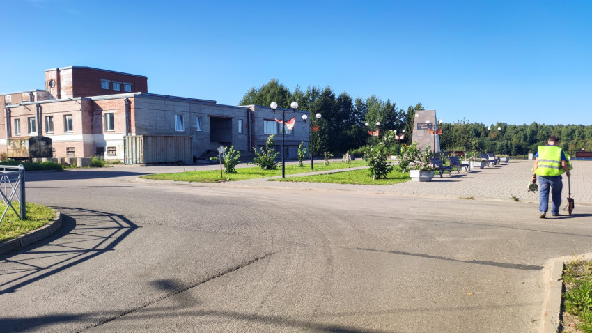 На перекрёстке у небольшого сквера рабочий с измерительным колесом проверяет длину участка дороги