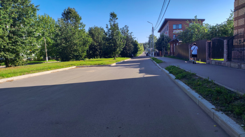 Пустая улица с новым асфальтом, тротуаром и зелёной полосой вдоль деревьев