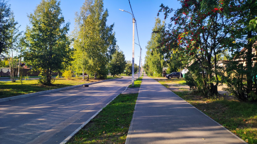Пешеходная дорожка вдоль ограды с деревьями и вытоптанной грунтовой тропой рядом