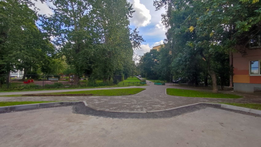 Двор с новыми дорожками из плитки и зелёной зоной между деревьями