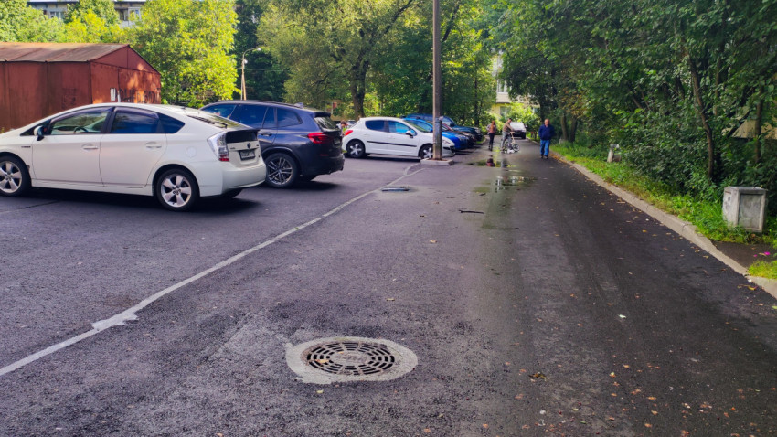 Парковка во дворе с рядами автомобилей и люком на мокром асфальте