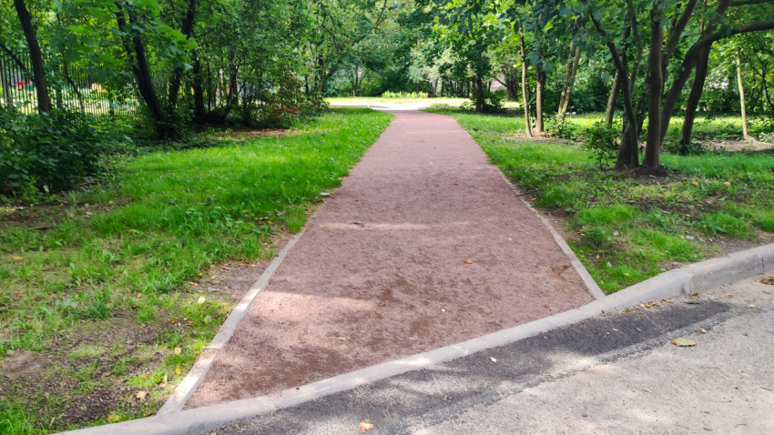 Красная дорожка из крошки тянется через зелёную зону между деревьями и бордюрами