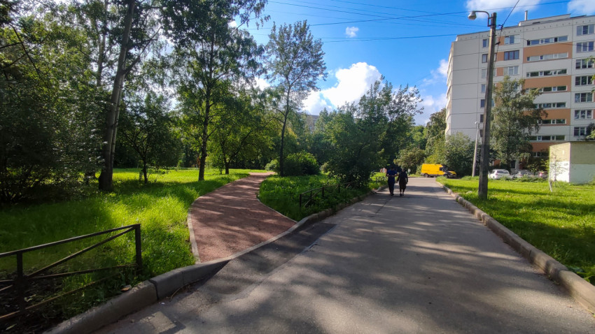 Дворовая территория с дорожками, деревьями и многоэтажным домом на заднем плане